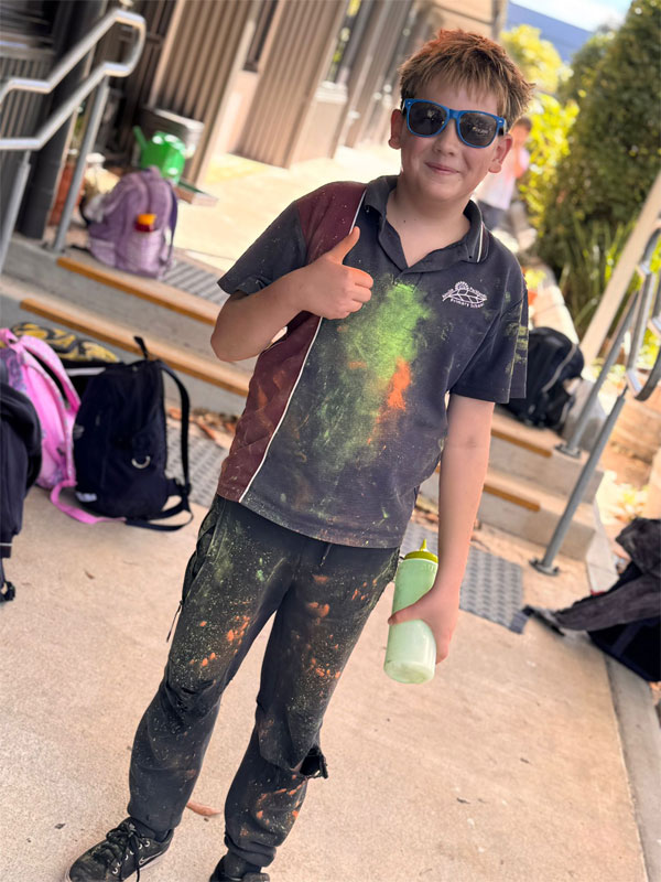 Smiling boy in an APPS sport uniform giving a thumbs up wearing sunglasses after a colour run